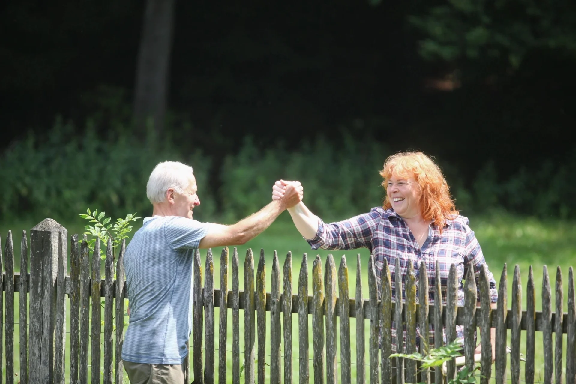Two people holding hands in front of a fence.